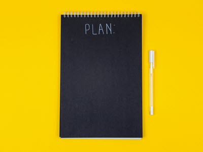 notebook with the word plan on the cover beside a pen