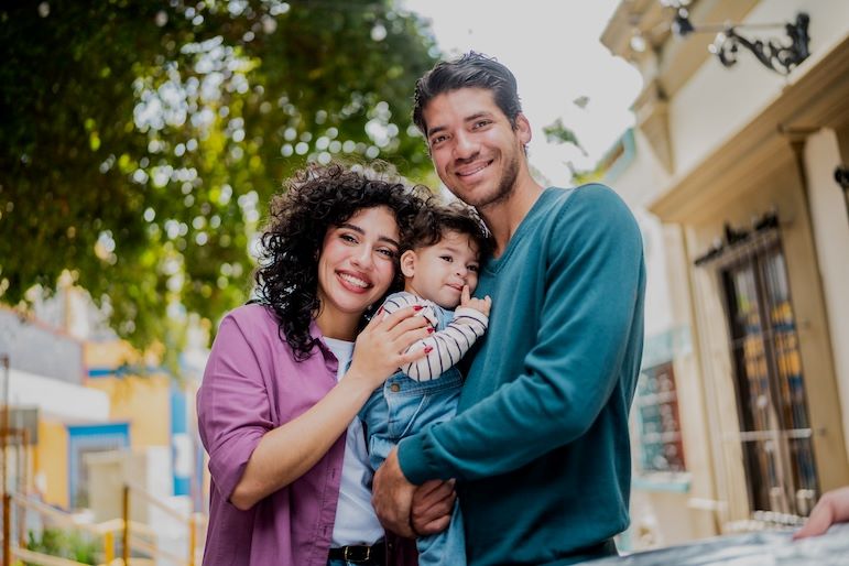 family of three smiling in front of home