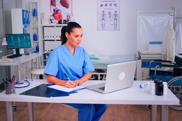 female nurse studying at laptop in exam room