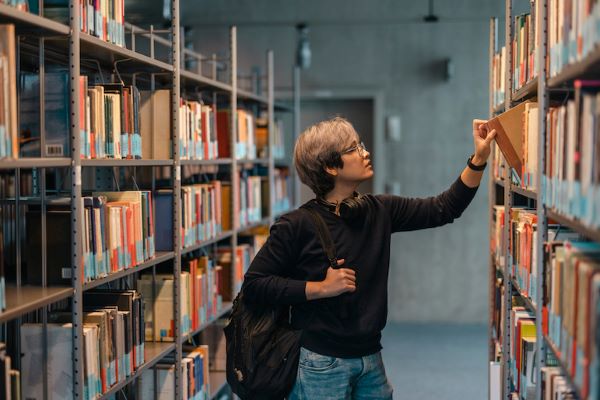 student pulling book off bookshelf in library