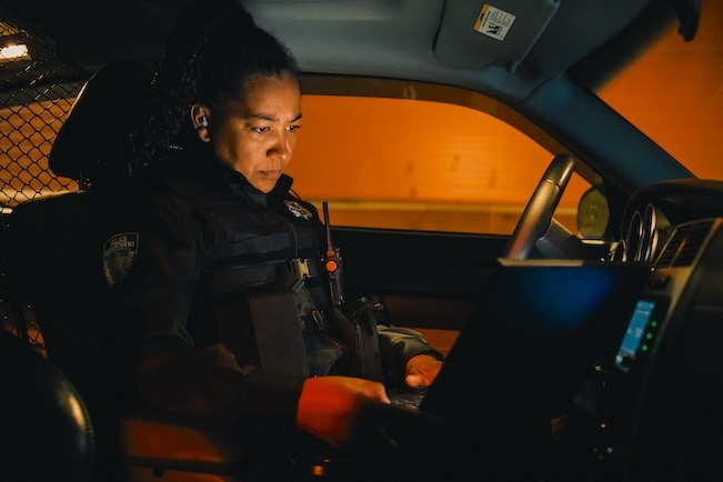 female officer sitting in police cruiser looking at laptop
